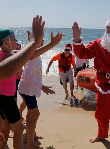 A surf life saver dressed as Santa Claus arrives to deliver gifts to children at Sydney's Coogee beach