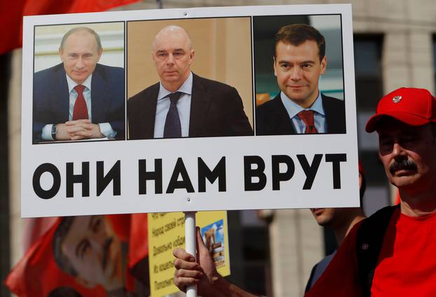 A man holds sign depicting Russian President Putin, FM Siluanov and PM Medvedev during a protest against a proposed increase of the retirement age in Moscow