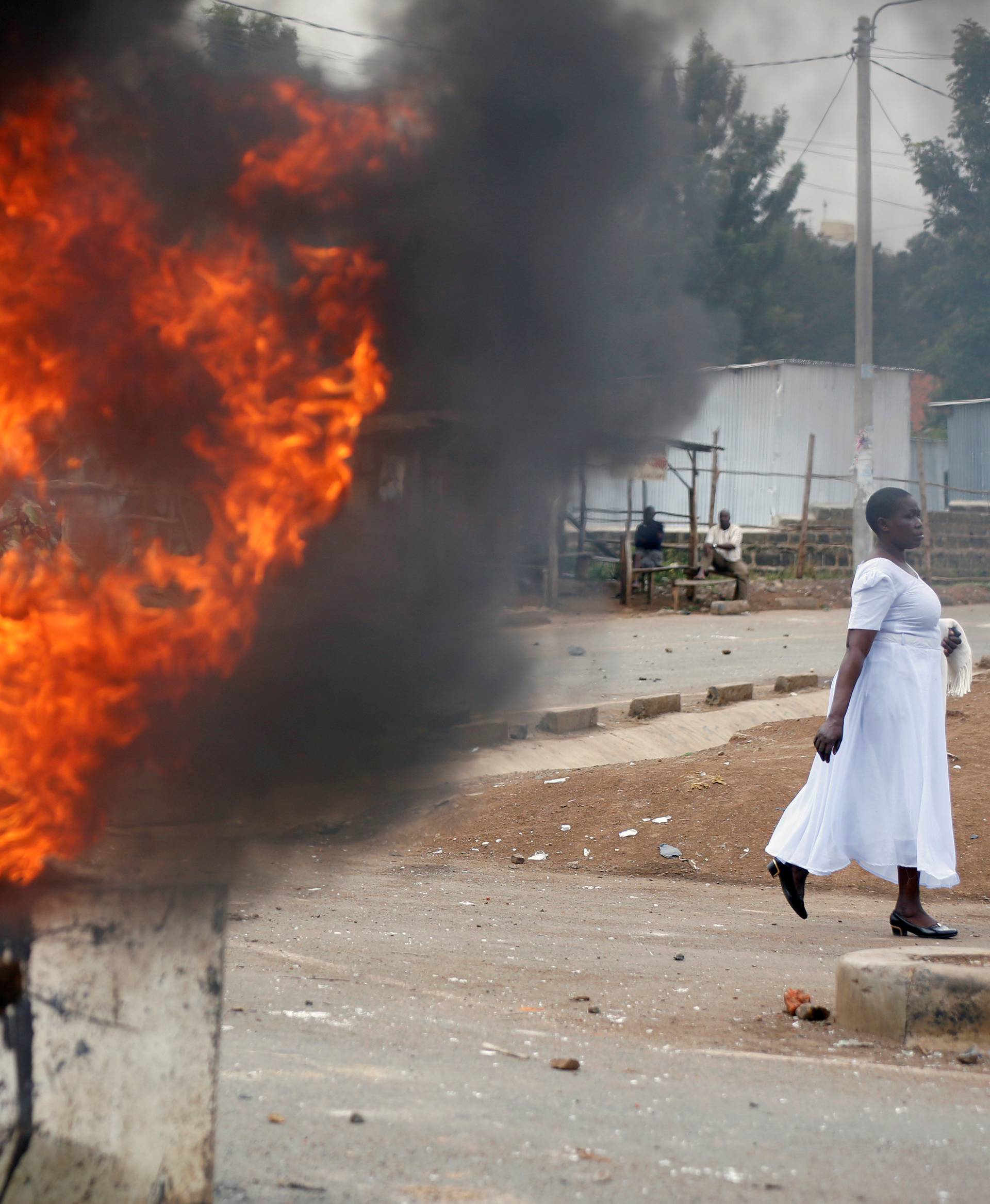 A woman walks past a burning barricades in Kisumu