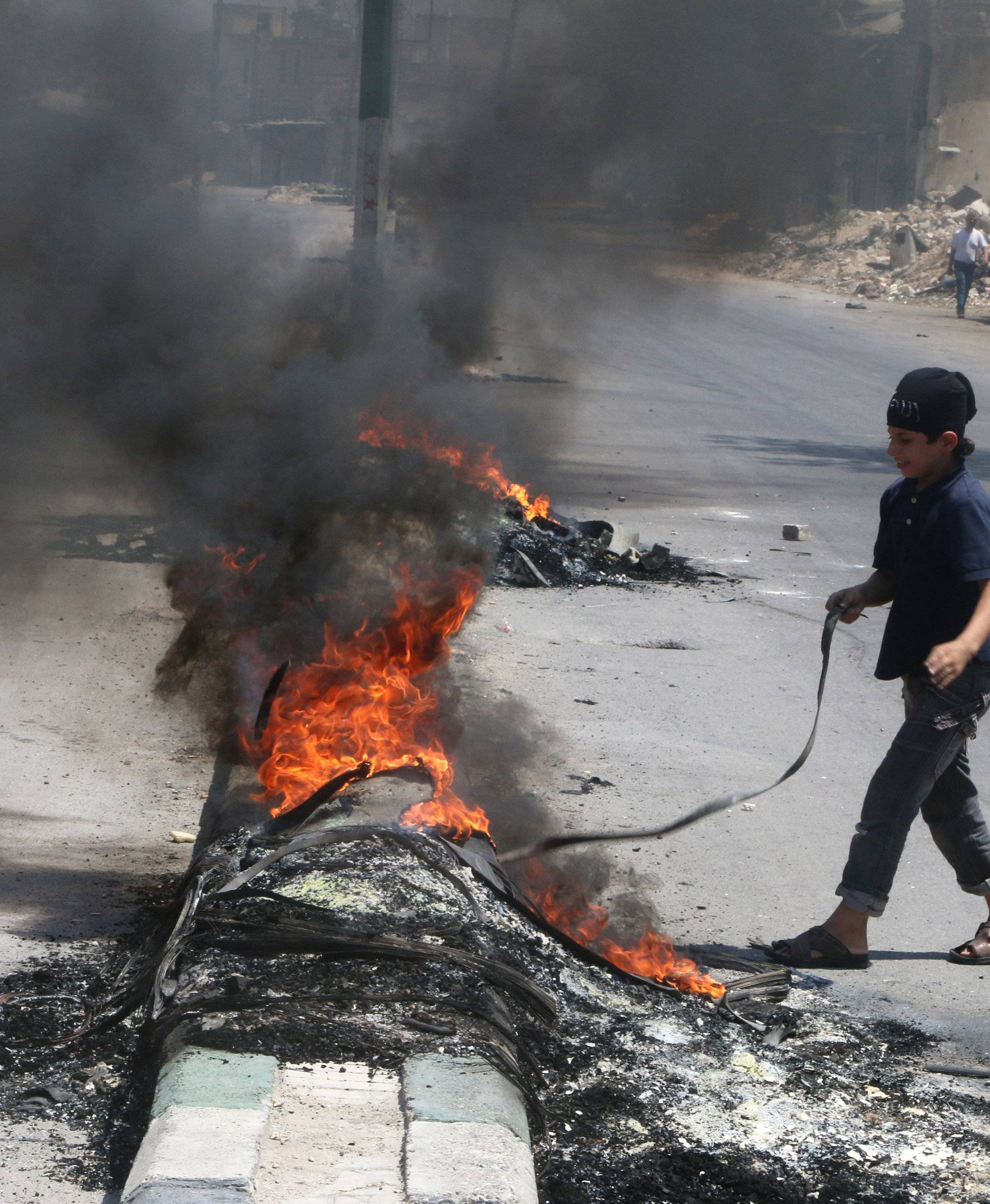 A boy inspects burning tyres, which activists said are used to create smoke cover from warplanes, in Aleppo
