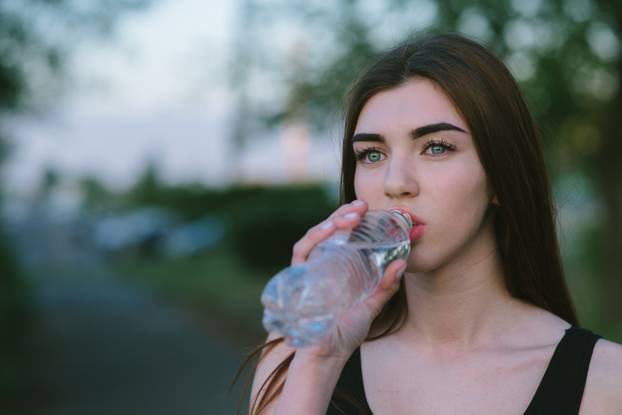 Portrait of a young athletic girl who is drinking refreshing water on a hot summer day. Sports lifestyle. Morning run.
