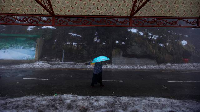 A woman holds an umbrella as she walks on a road during a cold winter day after snow fall in the hill-resort town of Murree, northeast of capital Islamabad