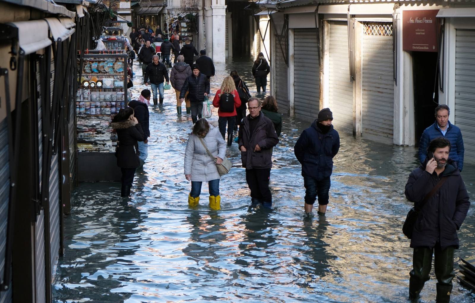 People walk through a flooded street during high tide in Venice