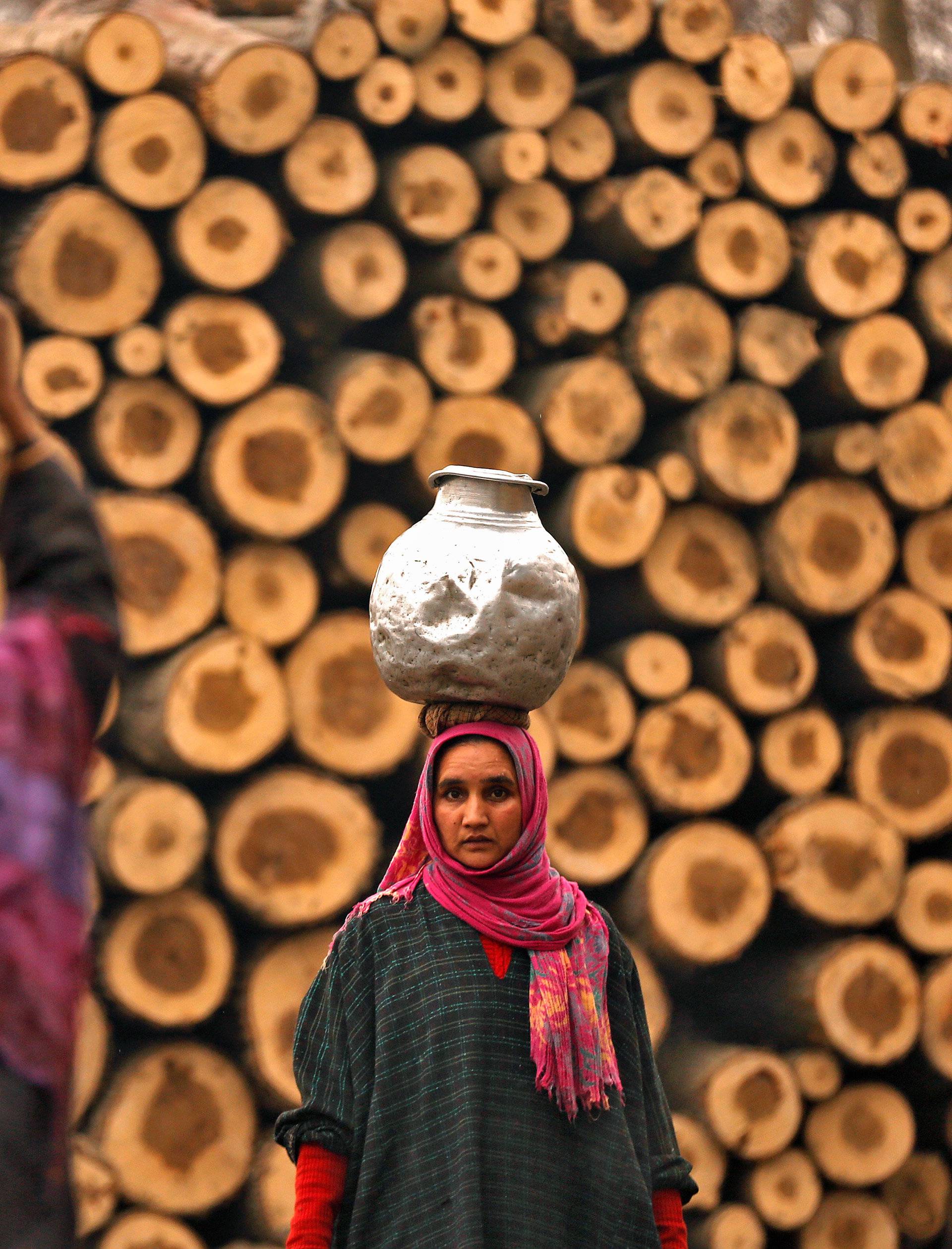 A woman carrying a metal pitcher filled with drinking water looks on in the outskirts of Srinagar