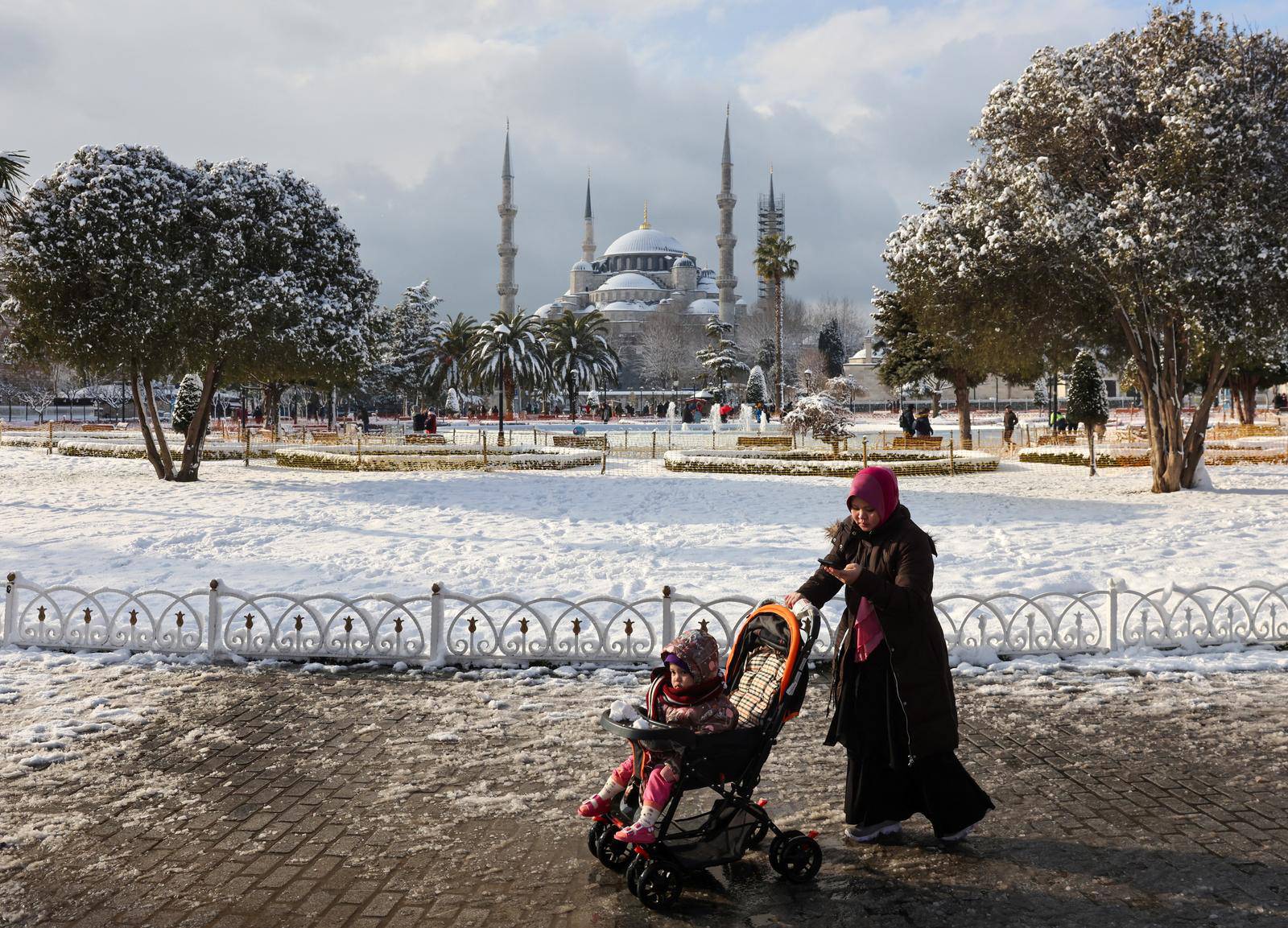 A tourist walks along Sultanahmet Square as Sultan Ahmet Mosque is seen in the background during a snowy day in Istanbul