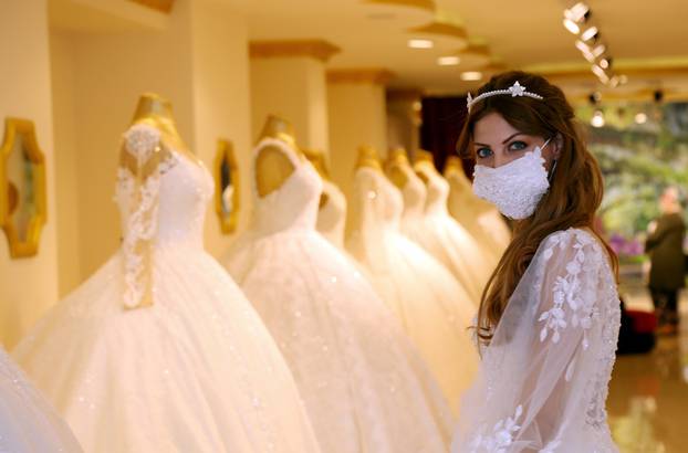 An employee presents a wedding dress with a mask at the Mezopotamya bridal gowns shop in Diyarbakir