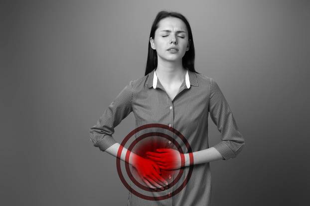 Woman showing discomfort while holding her stomach in a monochrome setting