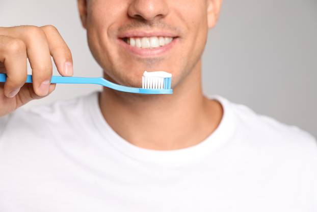 Man holding toothbrush with paste on light background, closeup