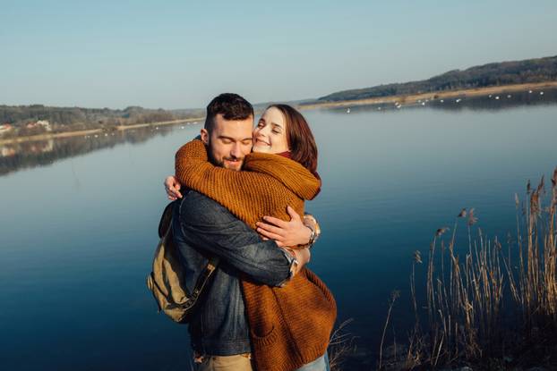 Travel and love. Happy young couple walking along the shore of blue lake in hipster clothes