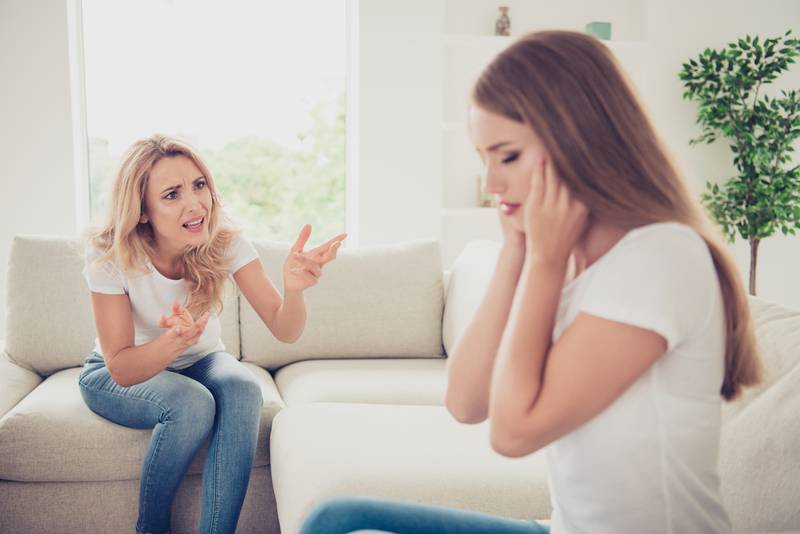 Close up photo unsatisfied two people mum and teenager daughter yelling fighting ignore not listen hide ears sick tired depressed wear white t-shirts jeans in bright flat sit on comfortable sofa