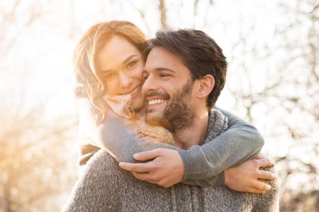 Closeup of smiling man carrying woman piggyback outdoor