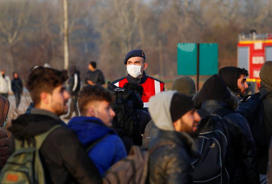 A Turkish gendarmerie officer wearing a face mask is seen as migrants walk next to the Turkey's Pazarkule border crossing with Greece's Kastanies, near Edirne