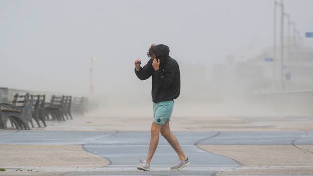 A man shields himself from the winds from Tropical Storm Isaias while walking on the boardwalk in the Rockaway area of Queens in New York