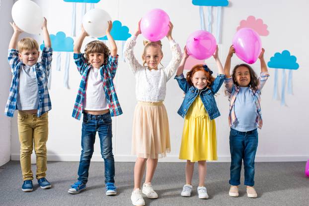 adorable multiethnic kids holding balloons and smiling at camera at birthday party 