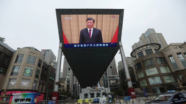 Medical workers in protective suits walks past a giant screen showing Chinese President Xi Jinping in Beijing
