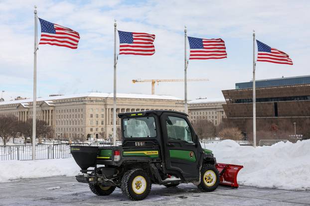 A John Deere vehicle equipped with a snow plow is parked in front of U.S. flags after a winter storm in Washington