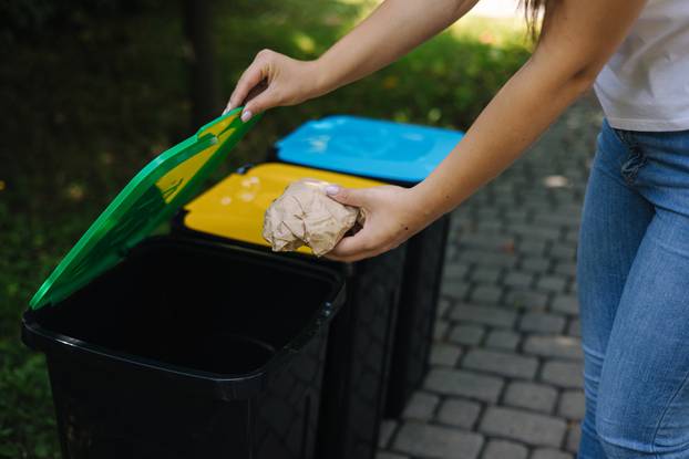 Closeup portrait woman hand throwing crumpled paper bag in recycling bin. Outdoors recycling bins different colours