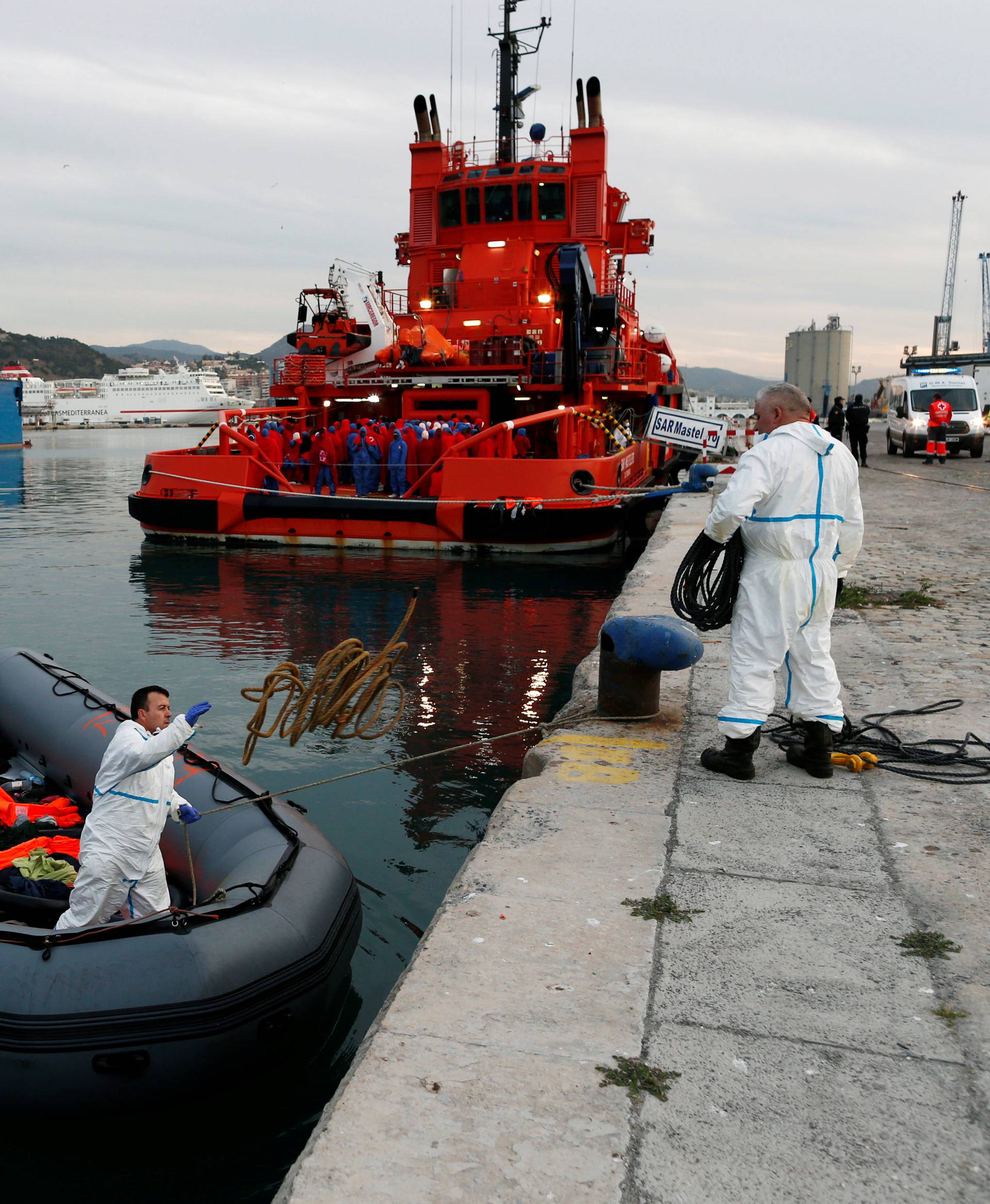 Migrants wait to disembark from a rescue boat as they watch as rescuers remove their floats and life-vests from a dinghy at dawn at the port of Malaga