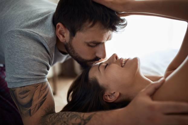 couple in bed being intimate with each other and kissing.
