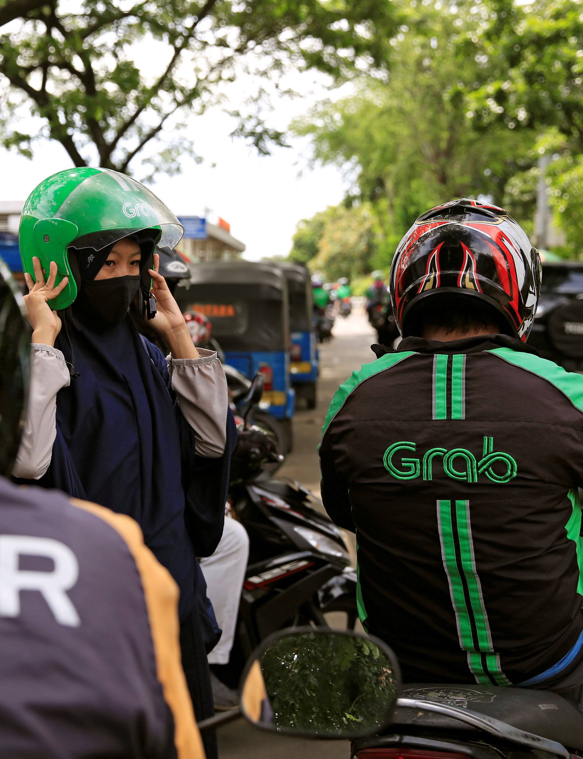 A passenger of Grab bike fixes her helmet next to Uber driver at Manggarai train station in Jakarta