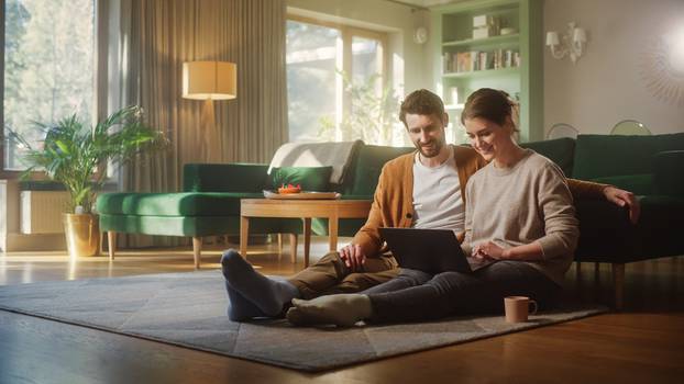 Couple,Use,Laptop,Computer,,While,Sitting,On,The,Living,Floor