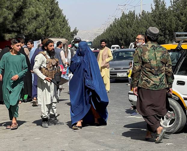 FILE PHOTO: Taliban forces block the roads around the airport, while a woman with Burqa walks passes by, in Kabul