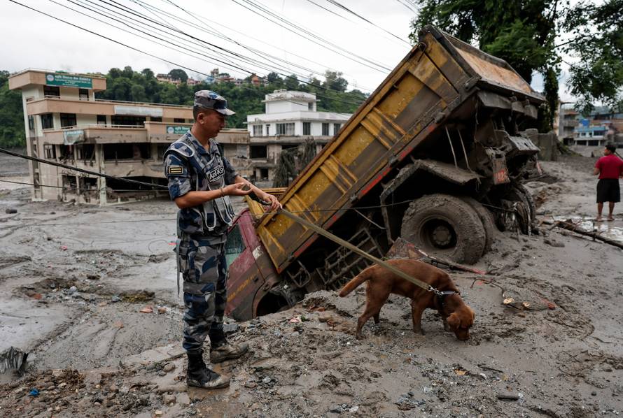 A security force member and his sniffer dog search for survivors following devastating floods, in Trishuli