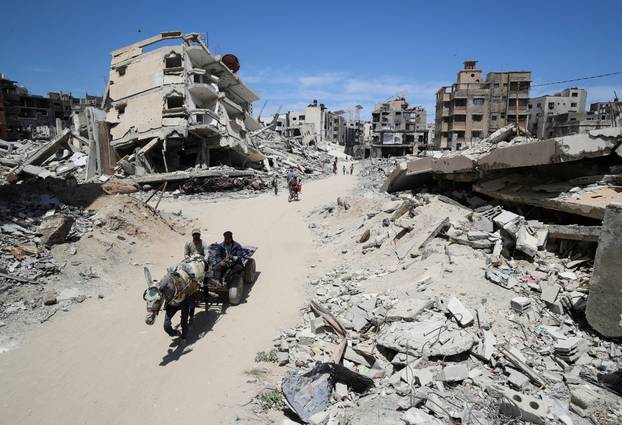 Palestinians ride a cart past the rubble of houses, in Gaza