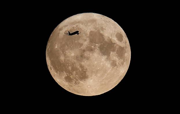 An aircraft flies over London and in front of the the super moon, know as the Blue Moon, in London