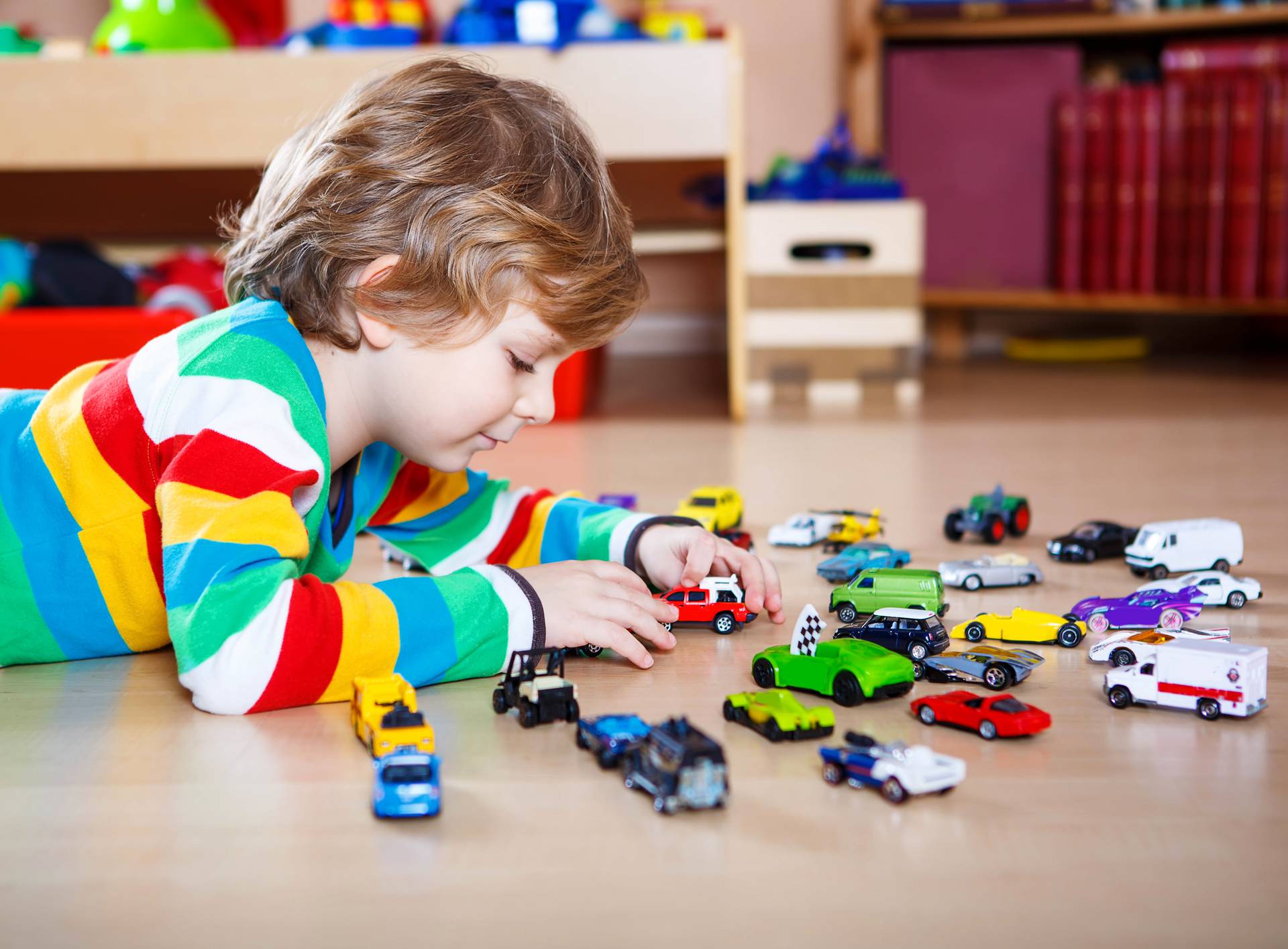 Little blond child playing with lots of toy cars indoor