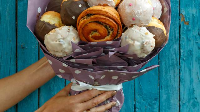 Girl holding a Bouquet made from different tasty buns and doughnuts on a blue wooden background