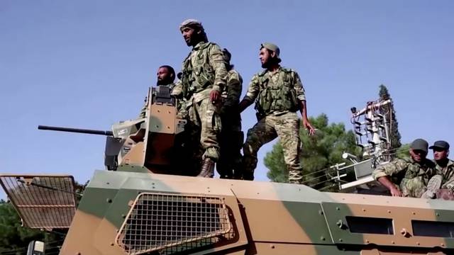 Syrian rebels stand on top of an armoured vehicle driving towards the border to cross into Syria, in Ceylanpinar