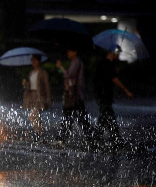 Pedestrians cross a street in heavy rain as a result of Typhoon Dujuan in Tokyo