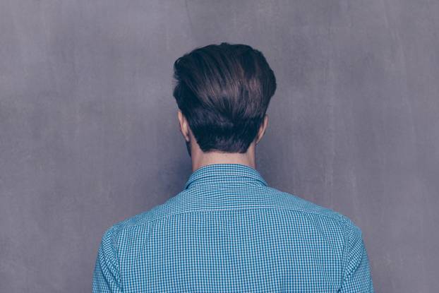 Back view of young guy in blue shirt  on gray background