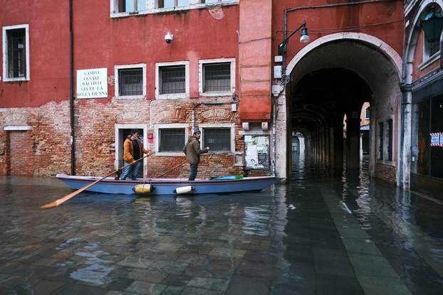 People ride a traditional boat in a flooded street during high tide as the flood barriers known as Mose are not raised, in Venice