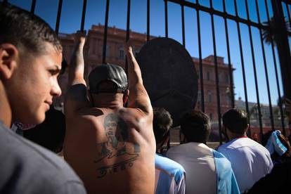 People stand outside the presidential palace Casa Rosada as they wait for the hearse carrying the casket of soccer legend Diego Maradona to drive past, in Buenos Aires
