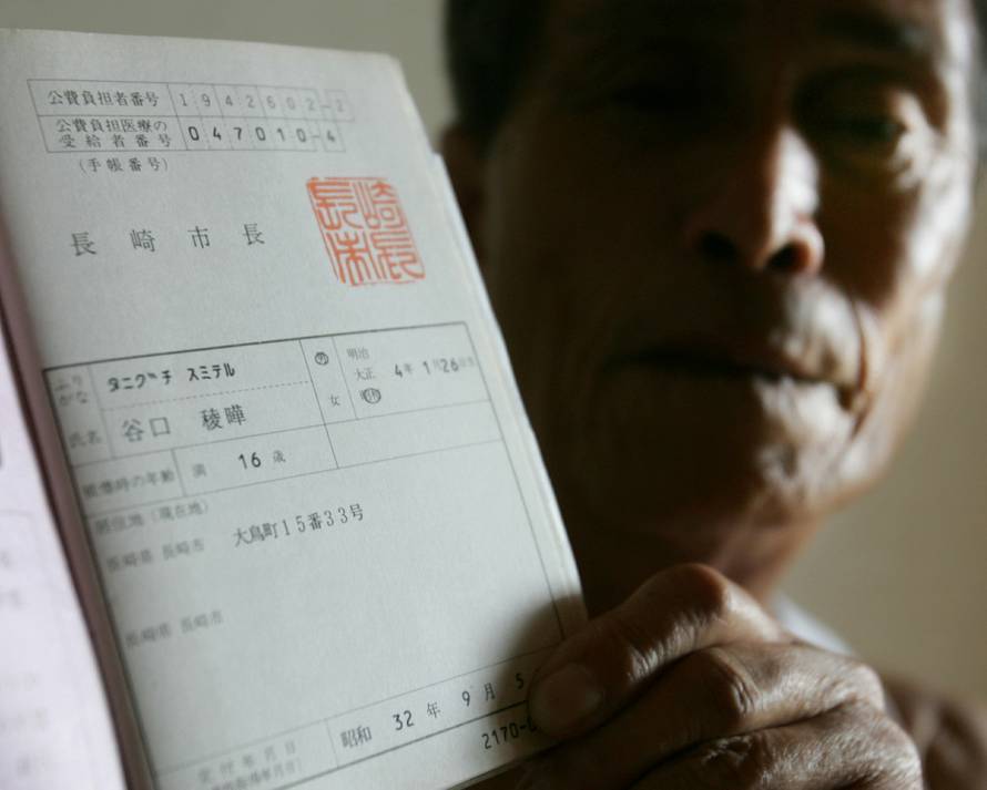 FILE PHOTO: Atomic bomb victim Sumiteru Taniguchi shows his bomb-survivor's health card at his home in Nagasaki
