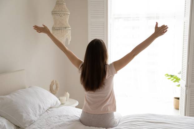 Back,View,Of,Optimistic,Young,Woman,Sit,On,Bed,In