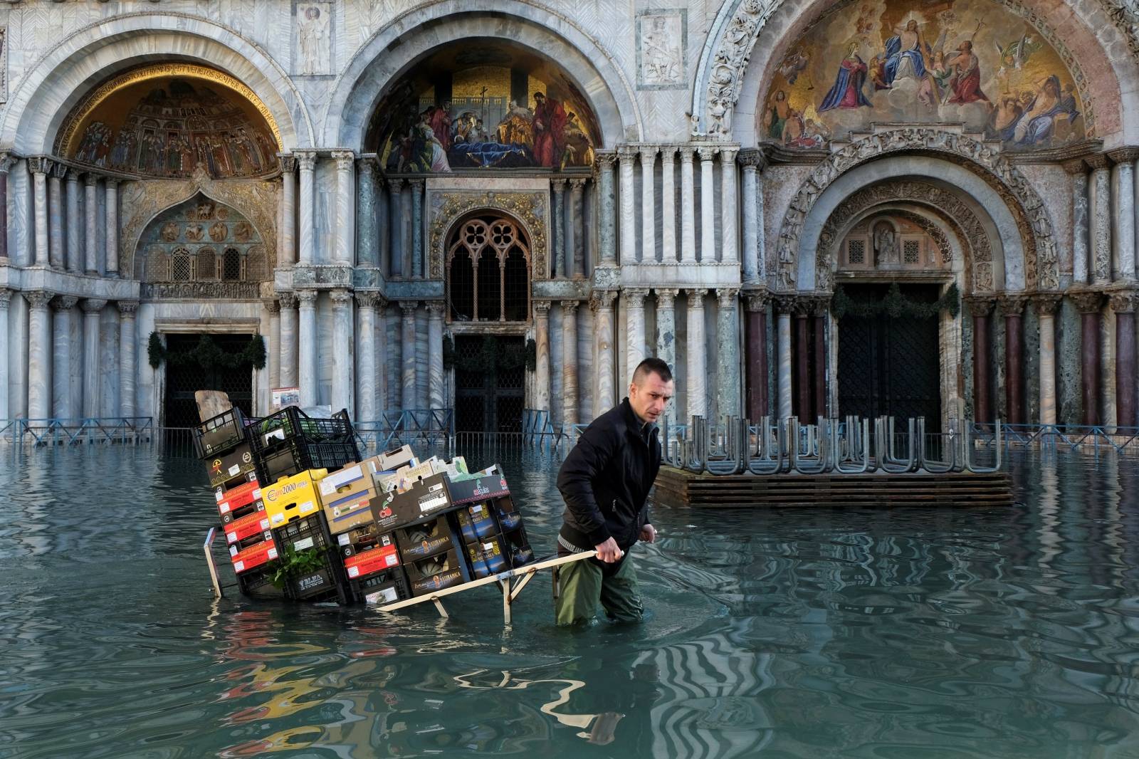 A man pulls a cart carrying fruits and vegetables through a flooded St. Mark's Square during high tide in Venice
