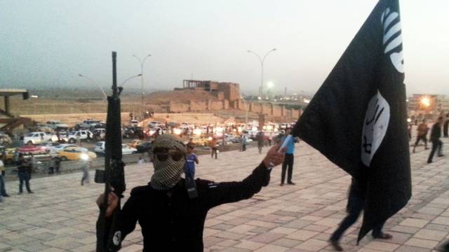 FILE PHOTO: A fighter of the ISIL holds a flag and a weapon on a street in Mosul