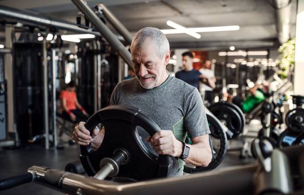 A senior man doing strength workout exercise in gym. Copy space.