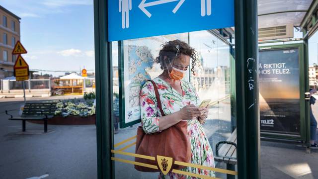 A woman wearing a face mask is seen in a bus stop next to an information sign asking people to keep social distance due to the outbreak of coronavirus disease (COVID-19), in Stockholm