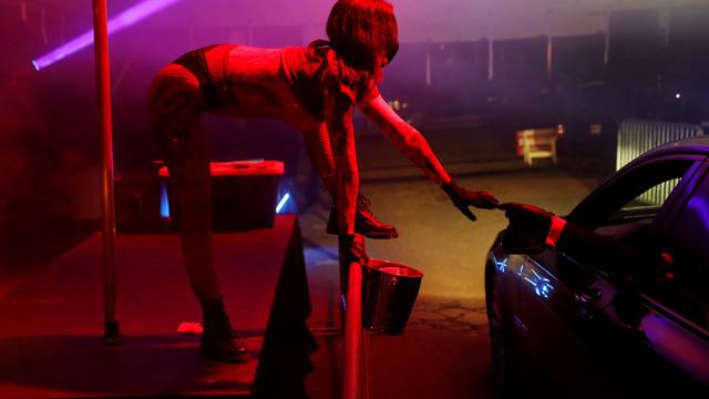 An exotic dancer wears personal protective equipment while taking a tip in a drive-through go-go dance tent at the Lucky Devil Lounge strip club in Portland