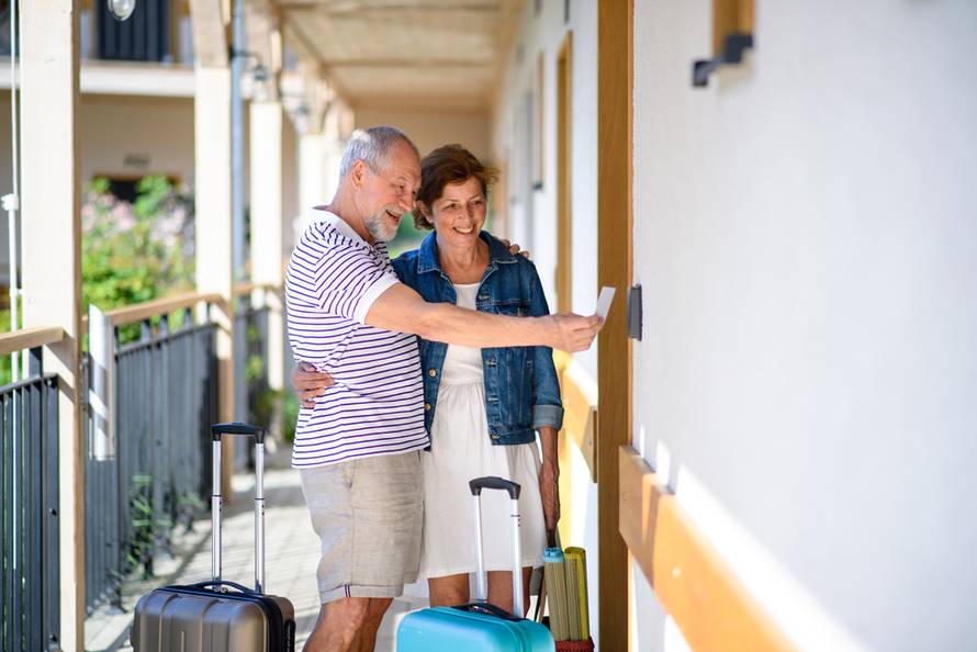 Senior,Couple,With,Luggage,Outside,Apartment,On,Holiday.