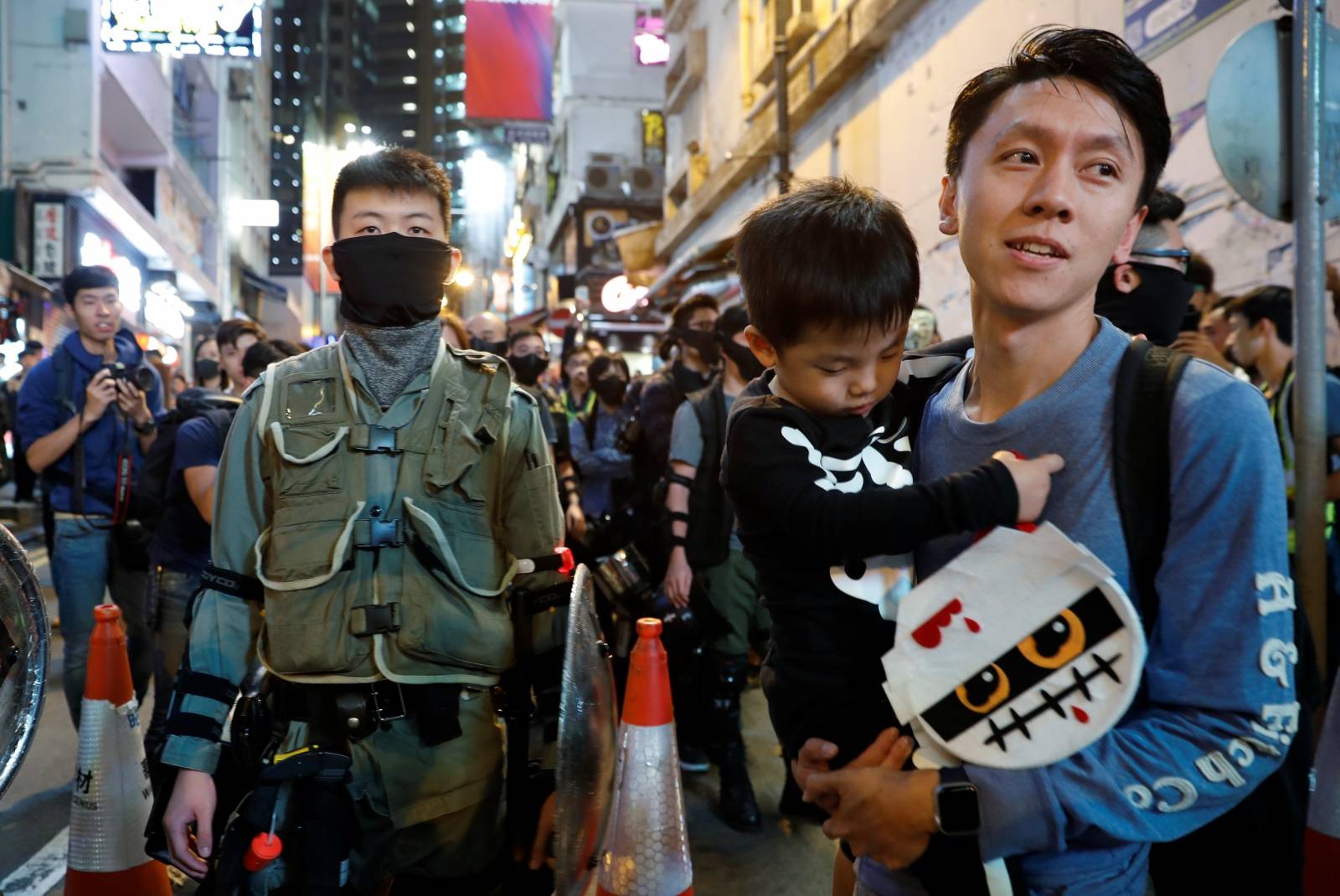A man holds his son with costume as he walks past a riot police during Halloween in Lan Kwai Fong