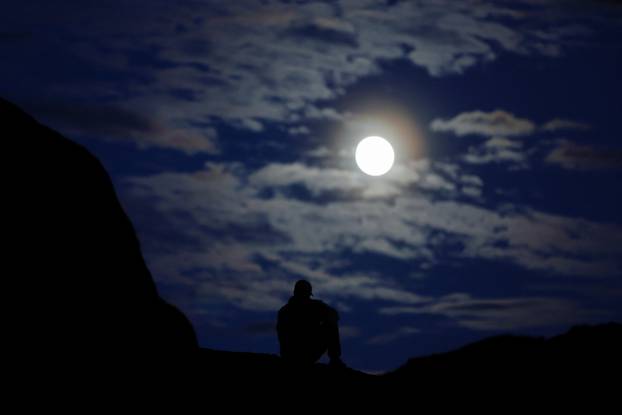 A man sits on a rock as the full moon, known as Hunter's moon and also the supermoon, rises in the Sahara desert outside Ouarzazate