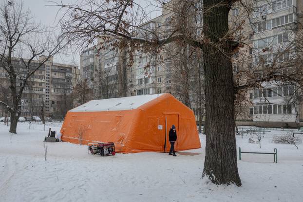 People warm up in a tent provided by emergency services for residents whose apartments are left without heating in Kyiv