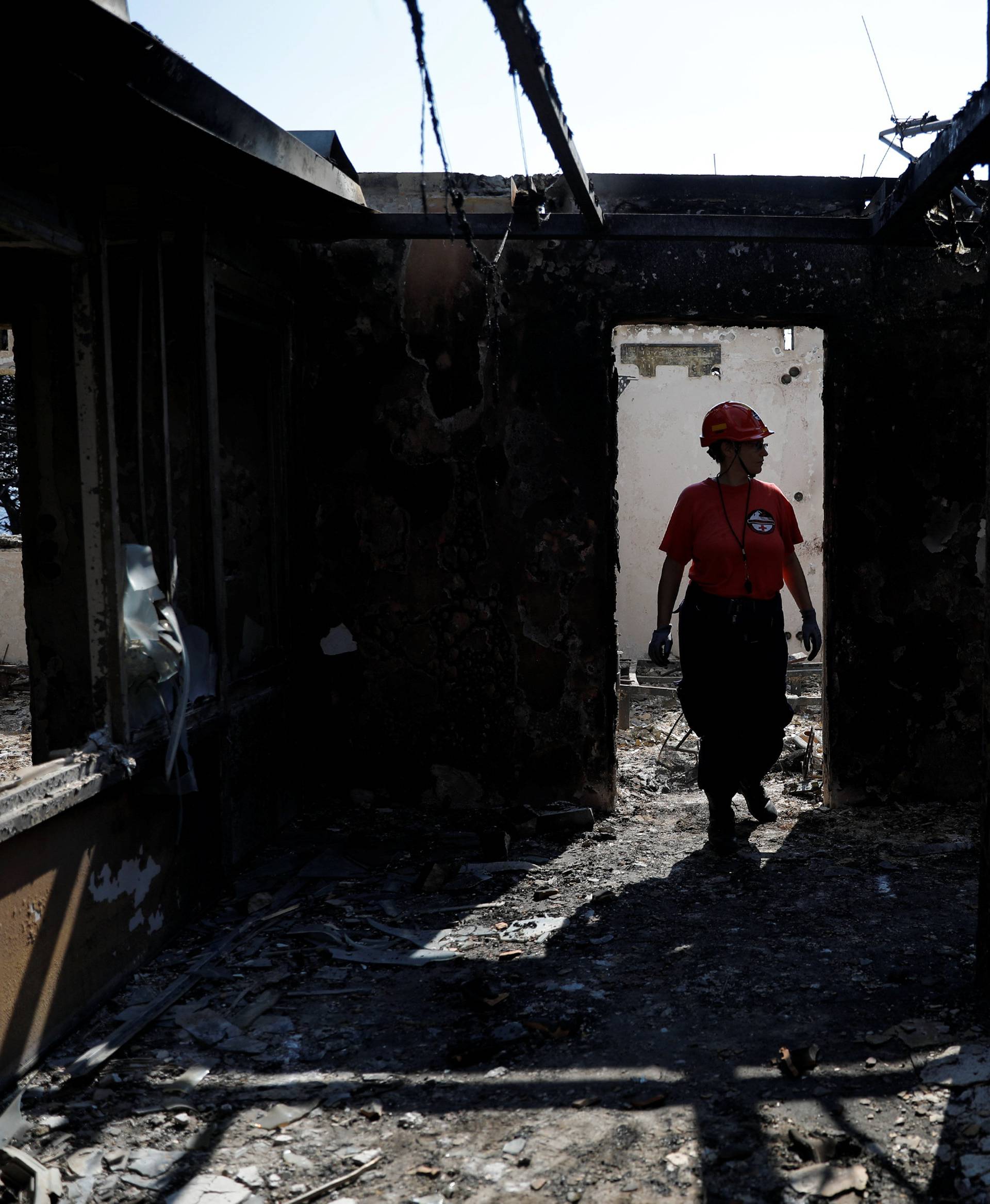 A member of a rescue team searches inside a destroyed building following a wildfire at the village of Mati