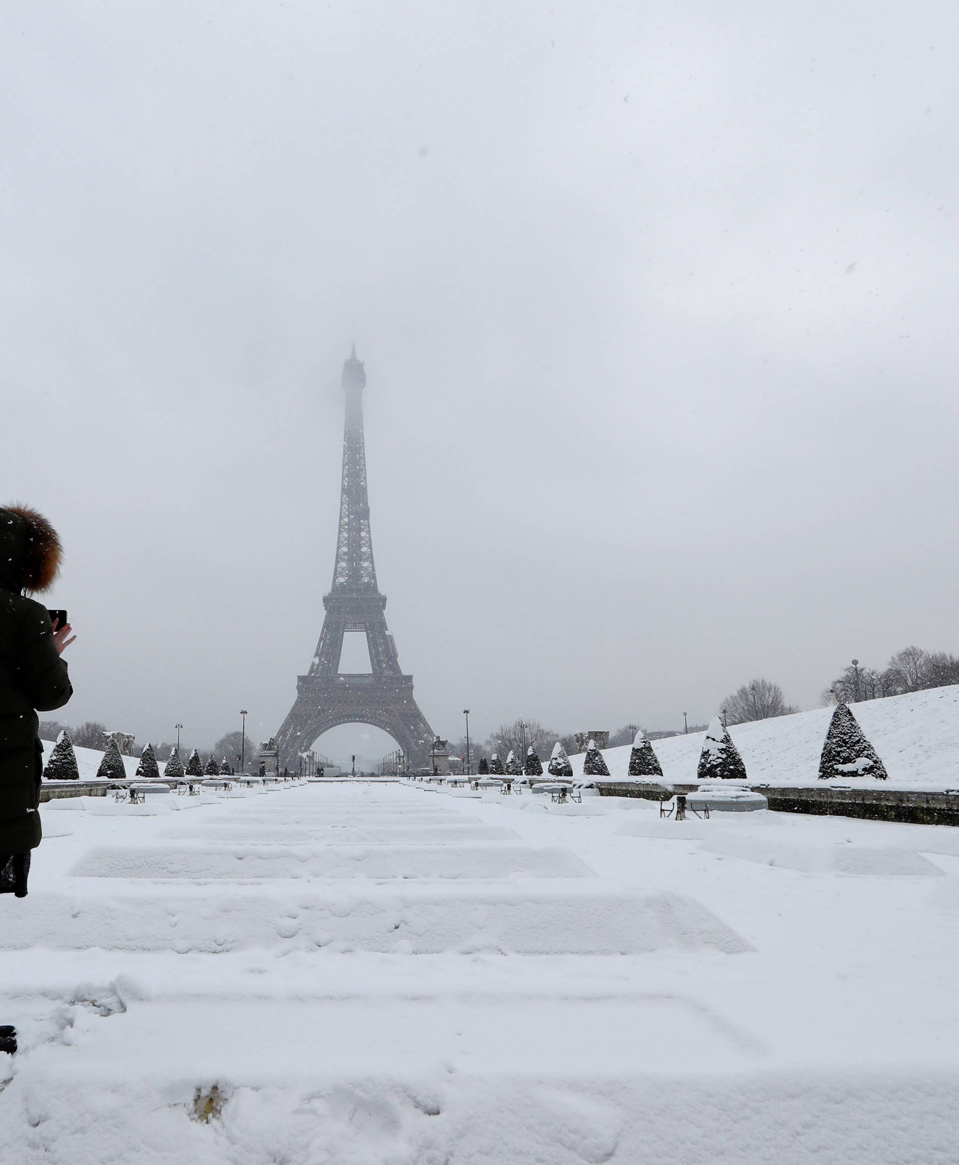 A woman takes pictures of the Eiffel Tower in Paris under the falling snow as winter weather continues in northern France