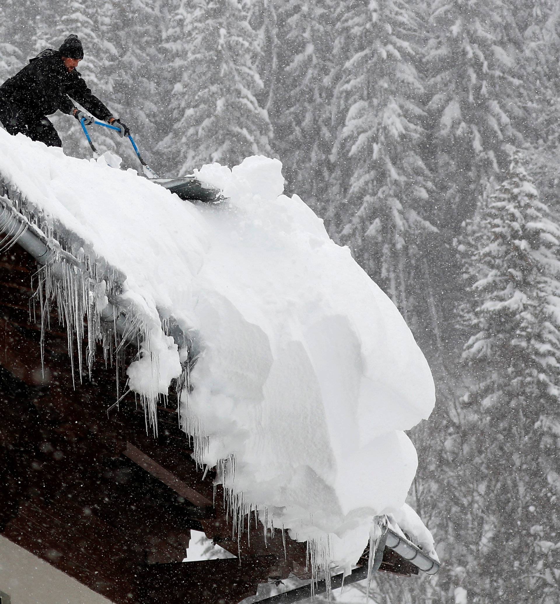 A man shovels snow on a rooftop during heavy snowfall in Filzmoos